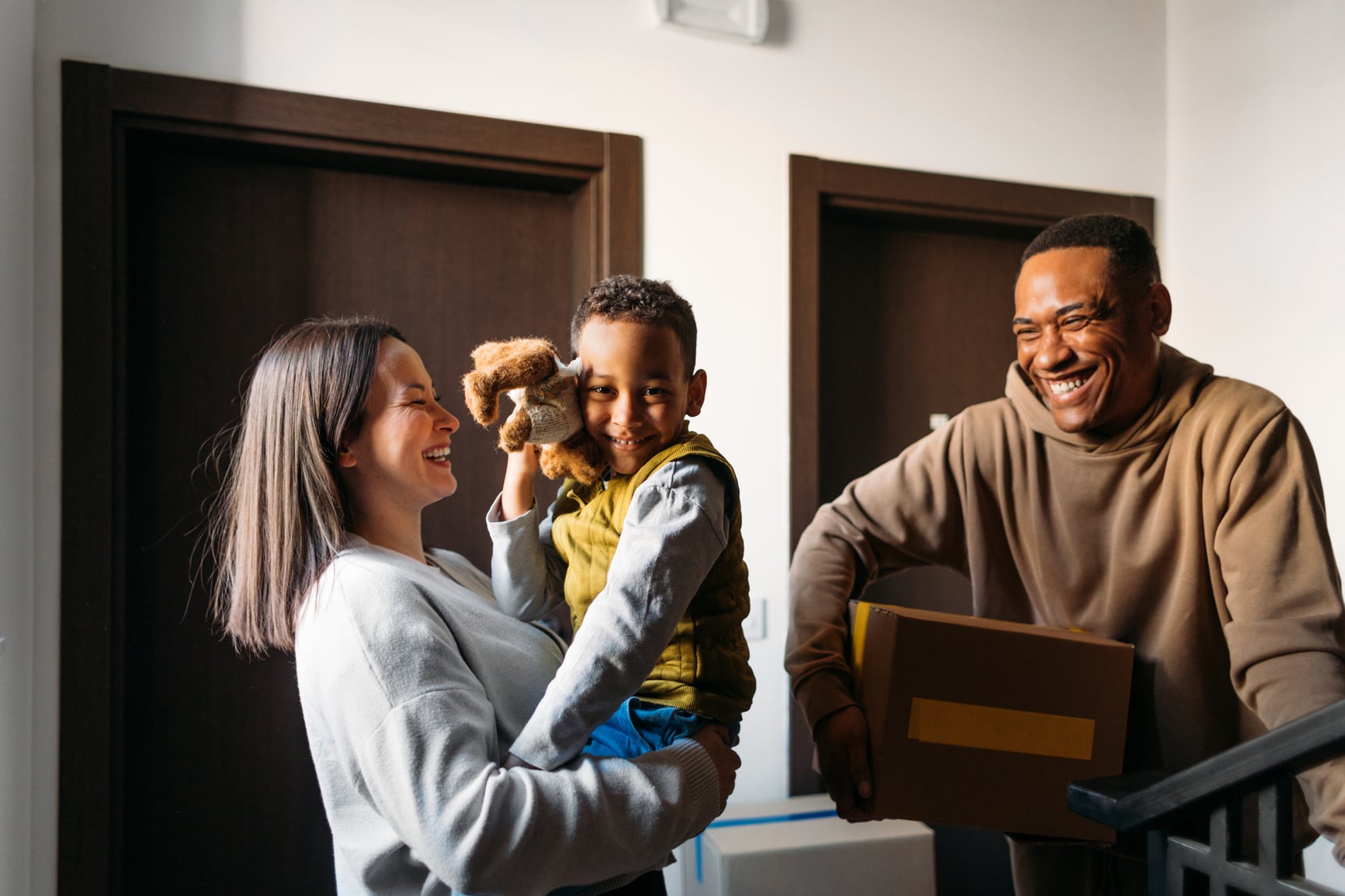 A smiling family of three on moving day, the father carrying a box